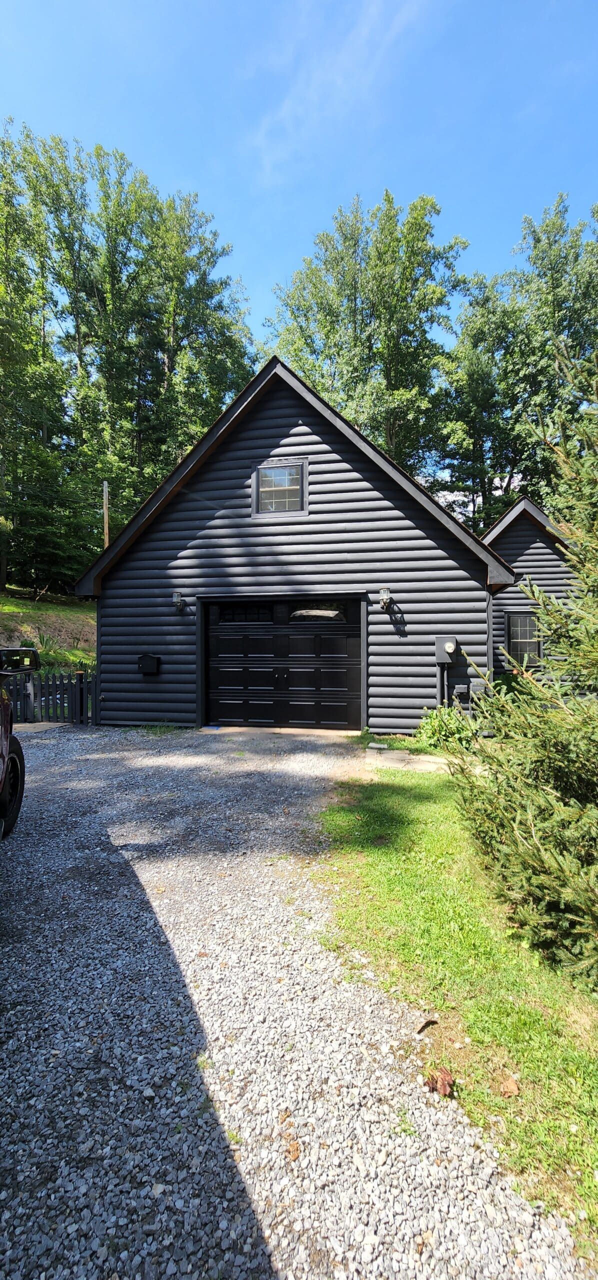 Black garage with trees and gravel driveway
