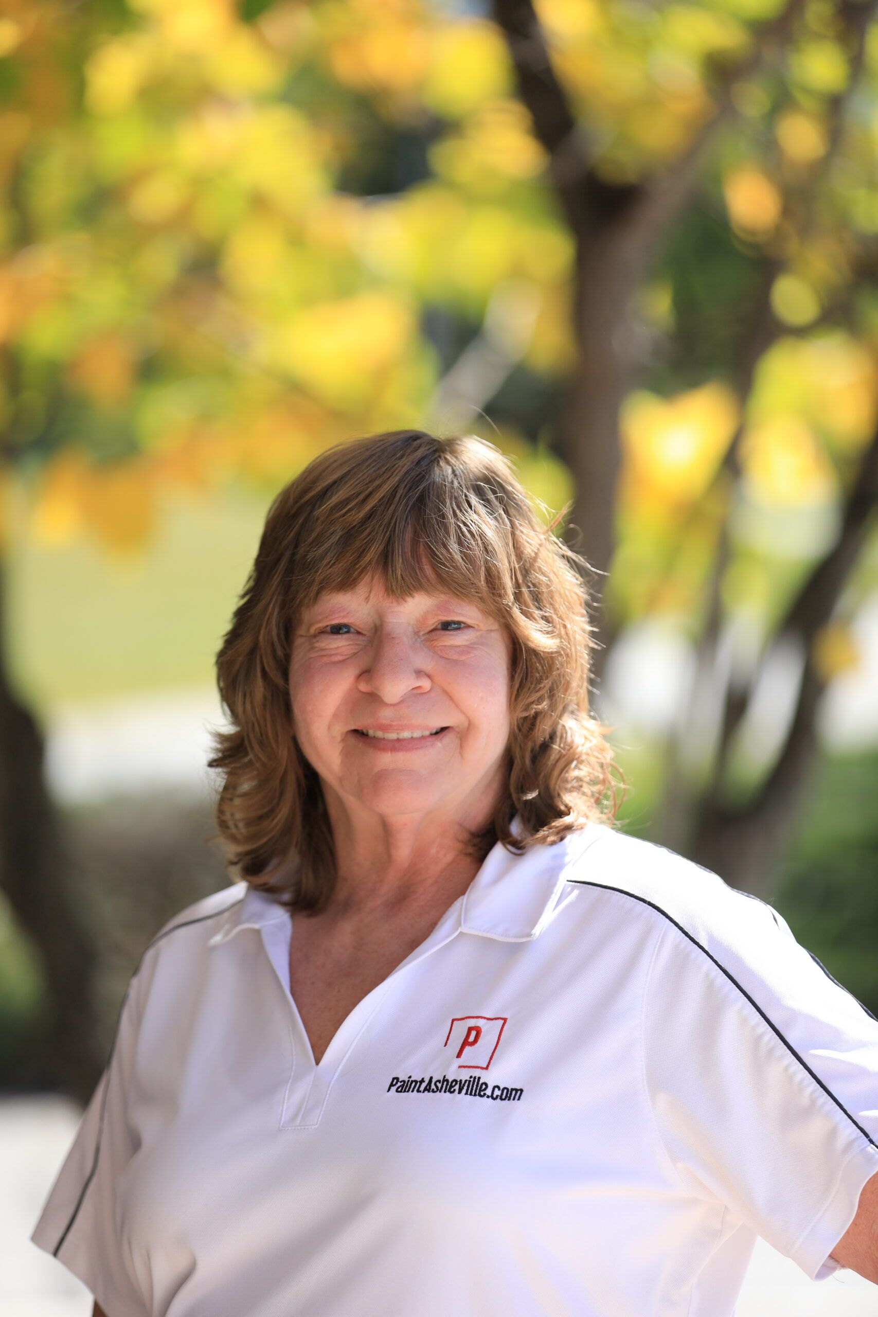 Smiling woman in white polo, autumn foliage